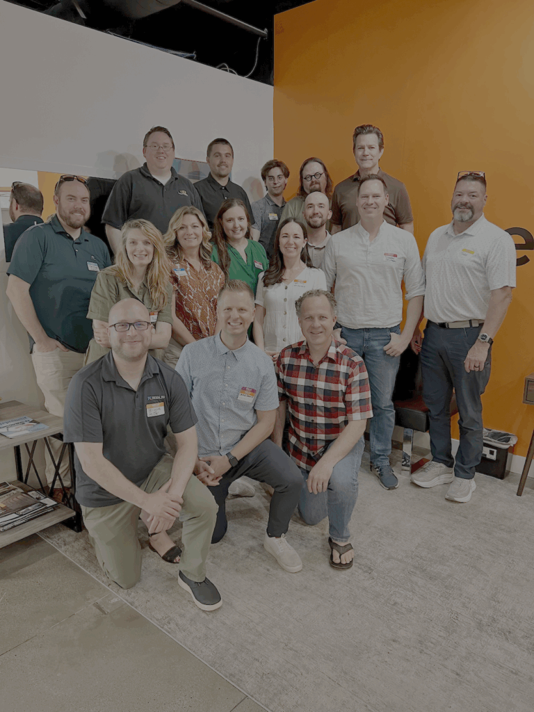 Group photo of approximately 20 people smiling and standing together inside an office with an orange wall featuring the green and orange "Pearagon" logo. The group is attending the Utah Marketing Group meeting, with several people wearing name tags.