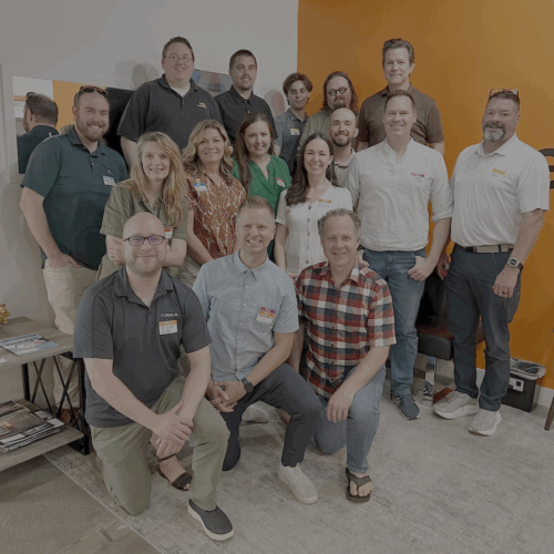 Group photo of approximately 20 people smiling and standing together inside an office with an orange wall featuring the green and orange "Pearagon" logo. The group is attending the Utah Marketing Group meeting, with several people wearing name tags.