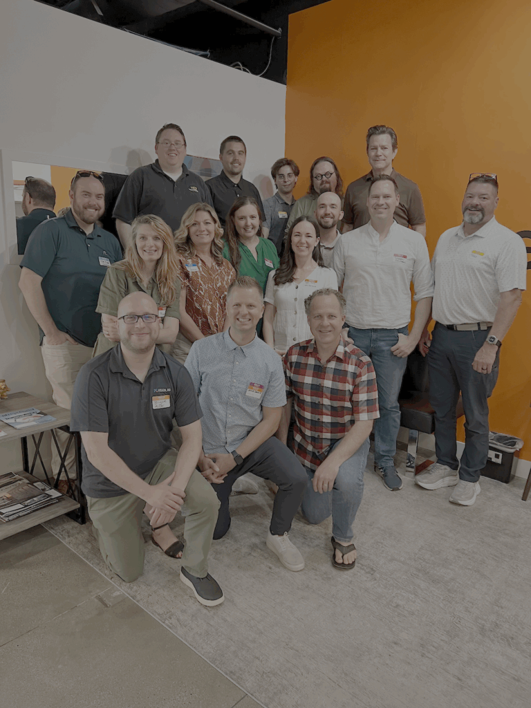 Group photo of approximately 20 people smiling and standing together inside an office with an orange wall featuring the green and orange "Pearagon" logo. The group is attending the Utah Marketing Group meeting, with several people wearing name tags.