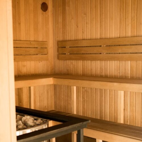 Interior of a wooden sauna with two-tiered bench seating and a metal stove filled with sauna stones in the foreground.