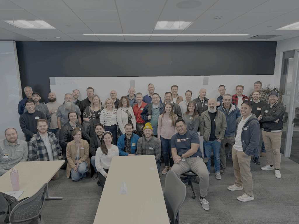 A large group of around 40 people posing together in a well-lit room. The group is smiling and dressed in casual to business-casual attire for a Utah Marketing Group meeting.