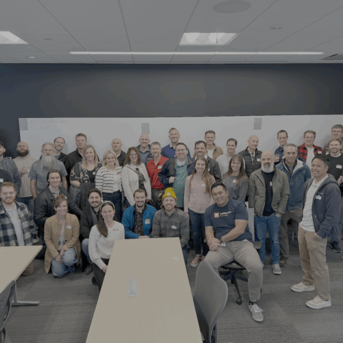 A large group of around 40 people posing together in a well-lit room. The group is smiling and dressed in casual to business-casual attire for a Utah Marketing Group meeting.