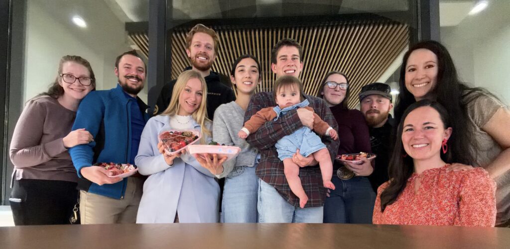 A group of 11 people standing in front of a table, holding heart-shaped charcuterie boxes they made at a class.