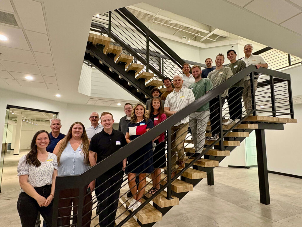 Attendees of a Utah Marketing Group networking event pose for a group photo on an indoor staircase in an office building. Participants line the stairs, smiling toward the camera.