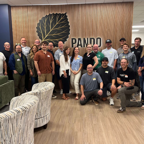 Group photo of Utah Marketing Group members gathered for a networking meeting at Pando Club, standing and kneeling together in front of the Pando logo and wood-paneled feature wall.